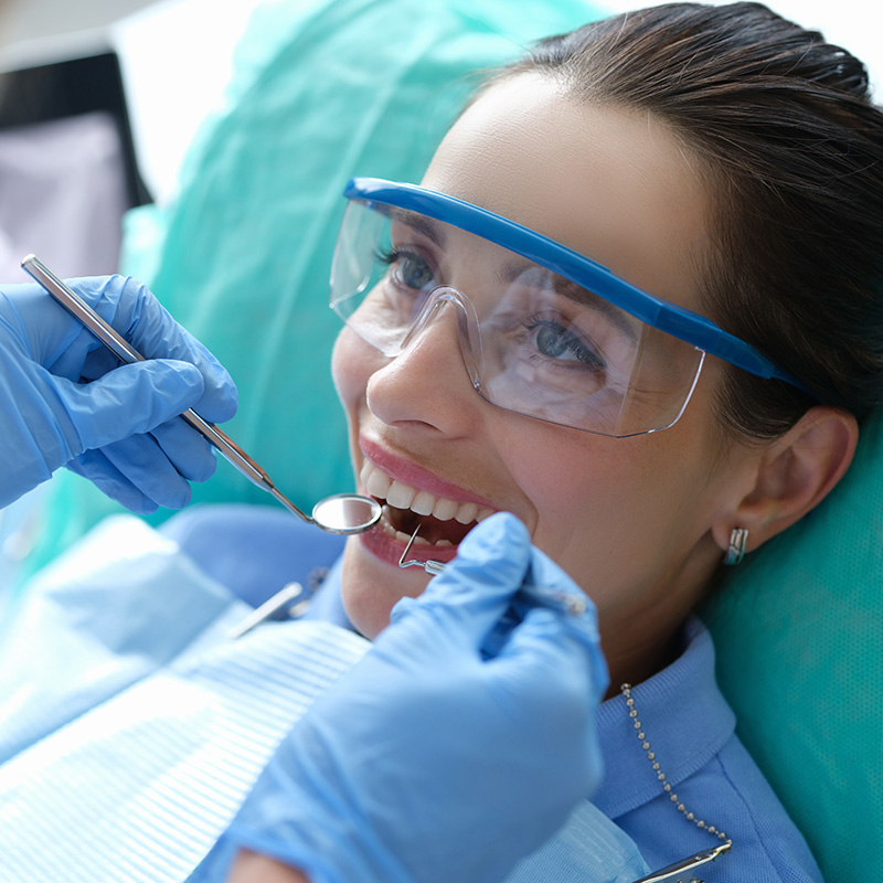 Woman Smiling with Safety Goggles on While teeth are being Checked by Dentist